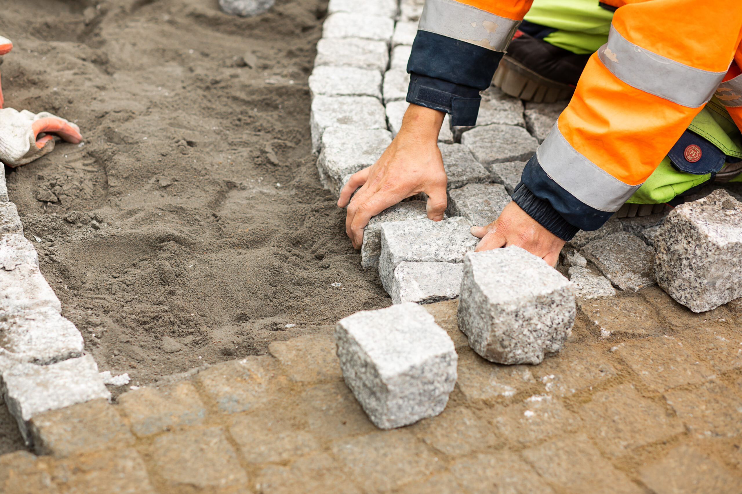 Maintenance work on paving with interlocking paving stones. Unrecognizable persons with building materials in hand, Concrete products, building industry for road or sidewalk construction.